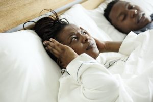 woman laying in bed next to husband and covering ears