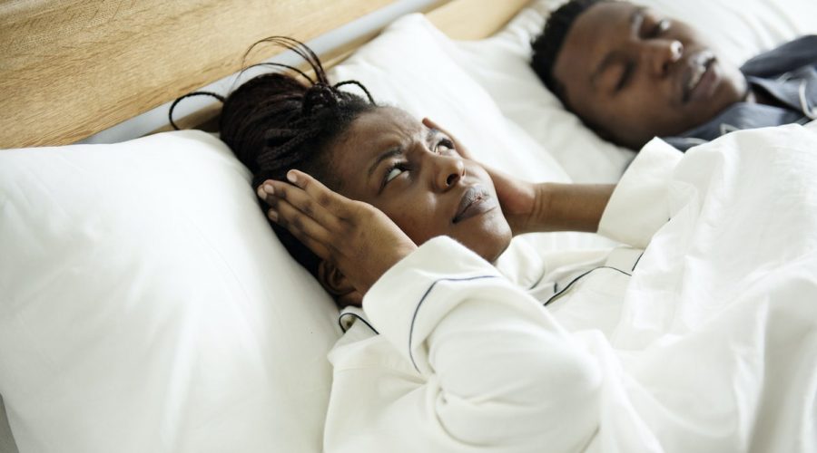 woman laying in bed next to husband and covering ears