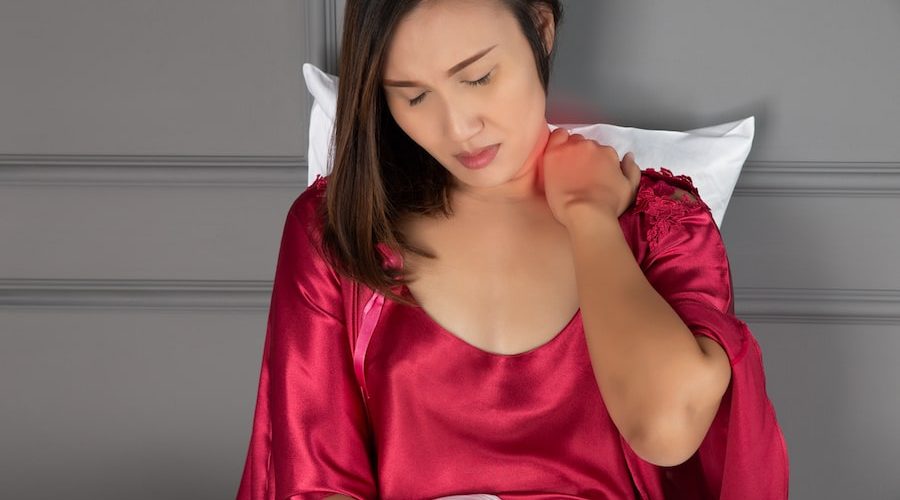 woman in red silk robe sitting up in bed rubbing her neck