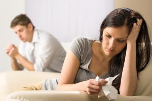 couple looking away from each other on the sofa, woman holding tissue and man looking serious