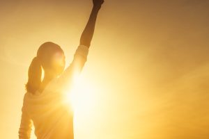 woman standing in front of bright sun with arm raised in the air triumphantly