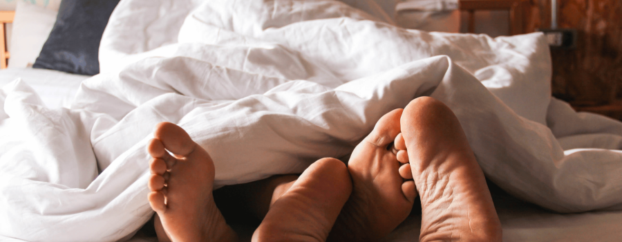Couple in bed under covers with feet visible.