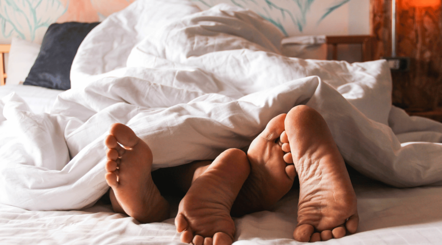 Couple in bed under covers with feet visible.