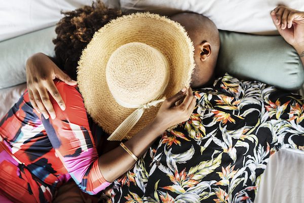 woman and man laying in bed embracing with straw hat covering faces