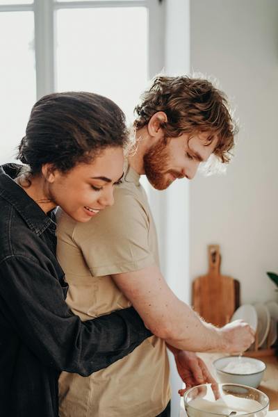 woman hugs man from behind while cooking together in kitchen