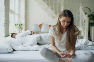 woman-sitting-on-bed-man-sleeping-behind-her